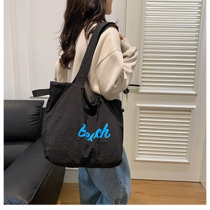 Model carrying a large black nylon tote bag with blue Beach lettering in a home setting