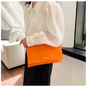 Detail of a bright orange clutch bag with a gold chain strap worn cross-body style