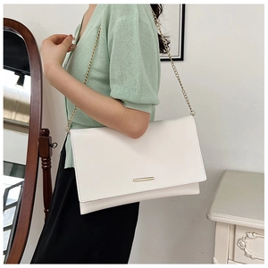 Close-up of white geometric envelope bag with gold hardware and elegant chain strap