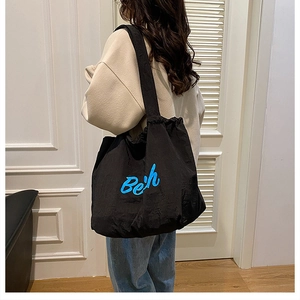 Close-up of black nylon tote bag with blue Beth embroidery and drawstring closure