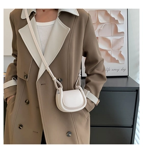 Detail of a minimalist cream mini saddle bag on a model wearing a brown trench coat