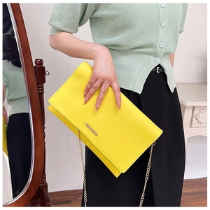 Fashionable bright yellow leather envelope clutch bag with gold chain strap on model