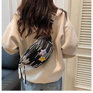 Detail of casual black chest bag with colorful star embroidery and striped strap on model