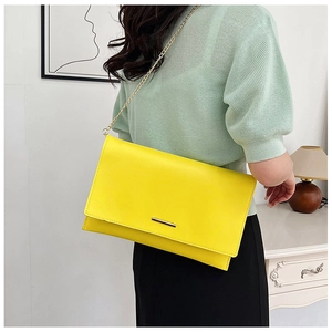 Detail of bright yellow envelope clutch bag with gold metal trim and chain strap