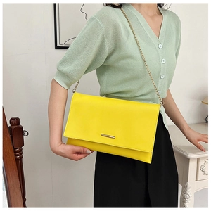 Detail of bright yellow crossbody bag with gold chain strap and metal bar trim