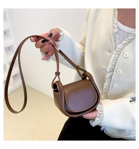 Detail of a dark brown mini saddle bag with gold metal buckle on a tweed jacket background