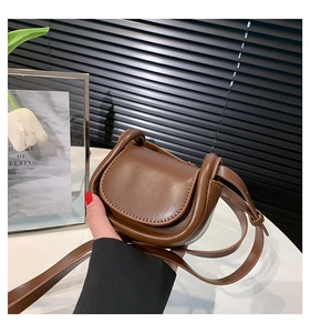 Detail of a brown PU leather mini saddle bag with an adjustable strap held by hand
