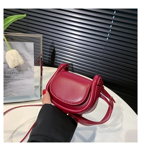 Macro shot of a deep red semi-circular saddle bag in smooth leather with a shoulder strap
