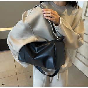 Minimalist black tote bag shown on model with wide strap and smooth PU leather finish