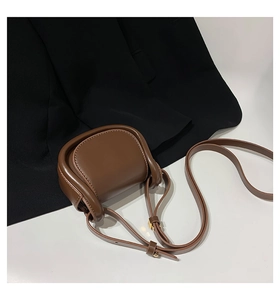 Detail of a brown leather mini saddle bag with gold hardware and adjustable strap