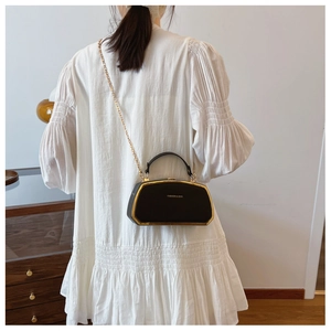 Elegante borsa a scatola nera con catena d'oro indossata da modella in abito bianco