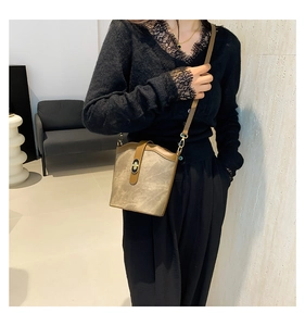 Close-up of khaki retro bucket bag featuring brown leather flap and gold twist lock clasp