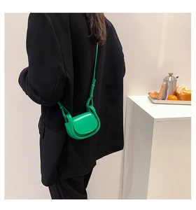 Detailed view of the bright green mini crossbody saddle bag worn with a black blazer