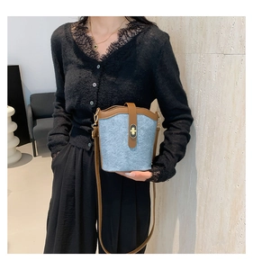 Detail of light blue denim bucket bag with brown leather trim and gold twist-lock closure