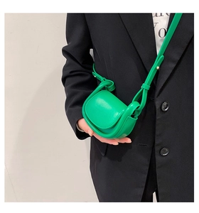 Close-up of a bright green mini saddle crossbody bag worn by a model with a black blazer