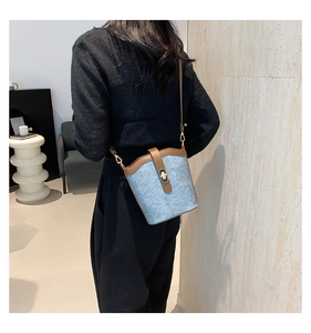 Detail view of blue felt bucket bag with brown leather trim on a model shoulder