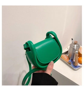 Detail of a green mini saddle bag with thick piping and adjustable leather strap