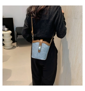 Detailed back view of a blue denim and brown leather bucket bag with an adjustable strap