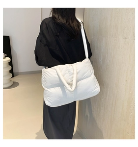 Rear view of a model wearing a large white quilted puffy tote bag with wide straps