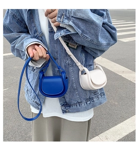 Close-up of mini matte leather saddle bags in royal blue and beige with thin shoulder straps
