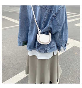 Detail of white mini semi-circle leather crossbody bag worn on denim jacket