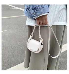 Detail of off-white faux leather mini saddle bag featuring a flap closure and slim strap