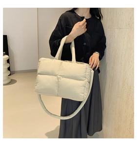 Detail of a beige quilted puffer tote bag with soft padded straps on a model