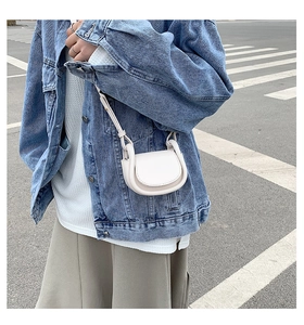 Detailed close-up of a mini off-white leather saddle bag worn by a model in denim