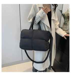 Quilted black padded tote bag with square stitching worn by a model in a modern room