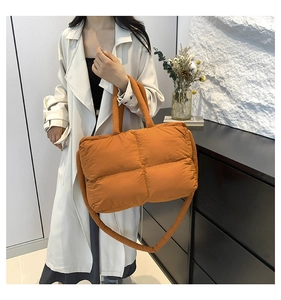 Quilted caramel orange puffer bag with wide strap styled on a white trench coat