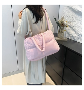 Pink quilted puffer shoulder bag with wide strap worn by model in minimalist indoor setting