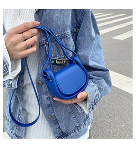 Close-up of a mini bright blue leather crossbody micro bag held by a person in denim