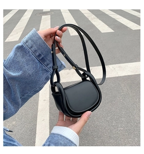 Detail of a mini black leather crossbody bag held by hand on an outdoor street