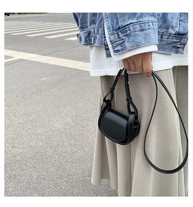 Close-up of a mini black leather crossbody bag with a curved flap and slim shoulder strap