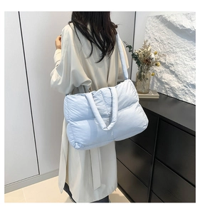 Detail view of a light blue quilted puffer tote bag shown on a model in a casual setting