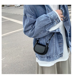 Detailed view of a black mini leather crescent shoulder bag worn by a girl on the street