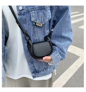 Close-up of a black leather mini crossbody bag worn by a model in a denim jacket