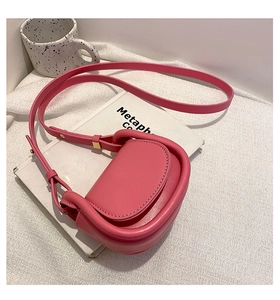 Detail view of pink faux leather saddle bag with gold buckle on white books and fabric