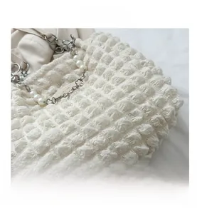 Detail van witte bubbeltas met parelband en goudkleurige bloemhangers voor dames
