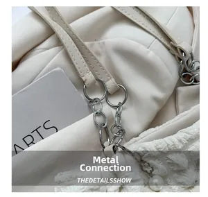 Detail van witte geplooide handtas met zilveren metalen ringen en parelbloem hanger