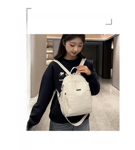 Detail eines cremefarbenen Nylon-Rucksacks mit metallischem Logo und glatter Reißverschlussstruktur