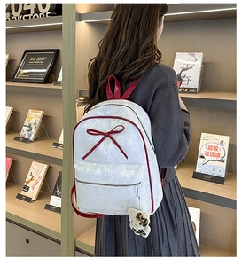 Detail of white leather backpack with red bow decoration and plush charm hanging on front