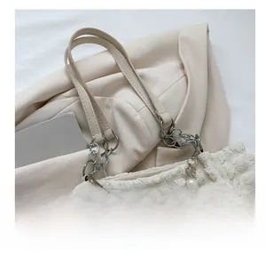Detail van de crème plissé shopper met parelaccenten en bloemvormige zilveren ketting