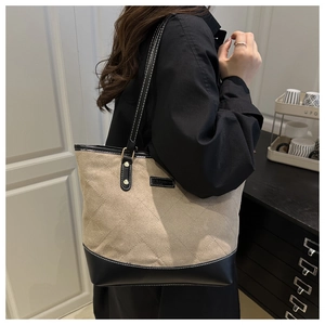 Side view of a large tote bag with beige quilting and black leather trim for work