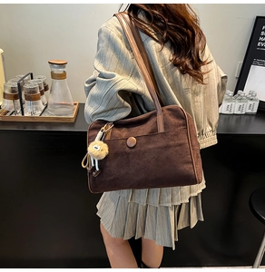Detailed view of deep brown suede tote with a decorative pom-pom on the shoulder strap