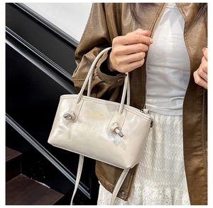 Detail of a beige PU leather tote bag featuring a gold fashion logo and knot strap accents