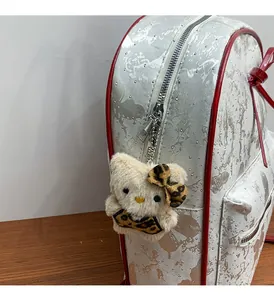 Detailed view of silver backpack with red piping and a white plush cat charm accessory