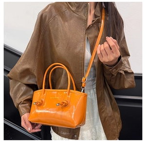 Detail of glossy orange tote bag featuring knotted accents and a leather shoulder strap