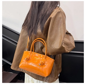 Detail of orange glossy tote bag showing metal knot decor and FASHION & BAGS lettering