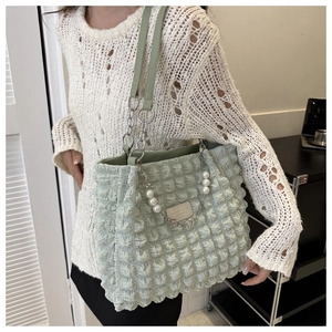 Detail van lichtgroene tas met bubbeltextuur, parelketting en lederen schouderband